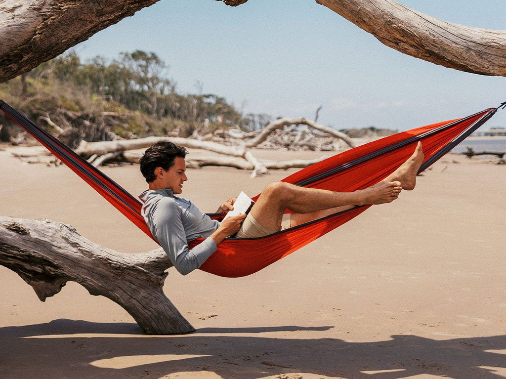 Man sitting in hammock on beach reading.