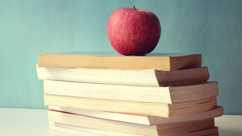 stack of books on teacher's desk with apple on top