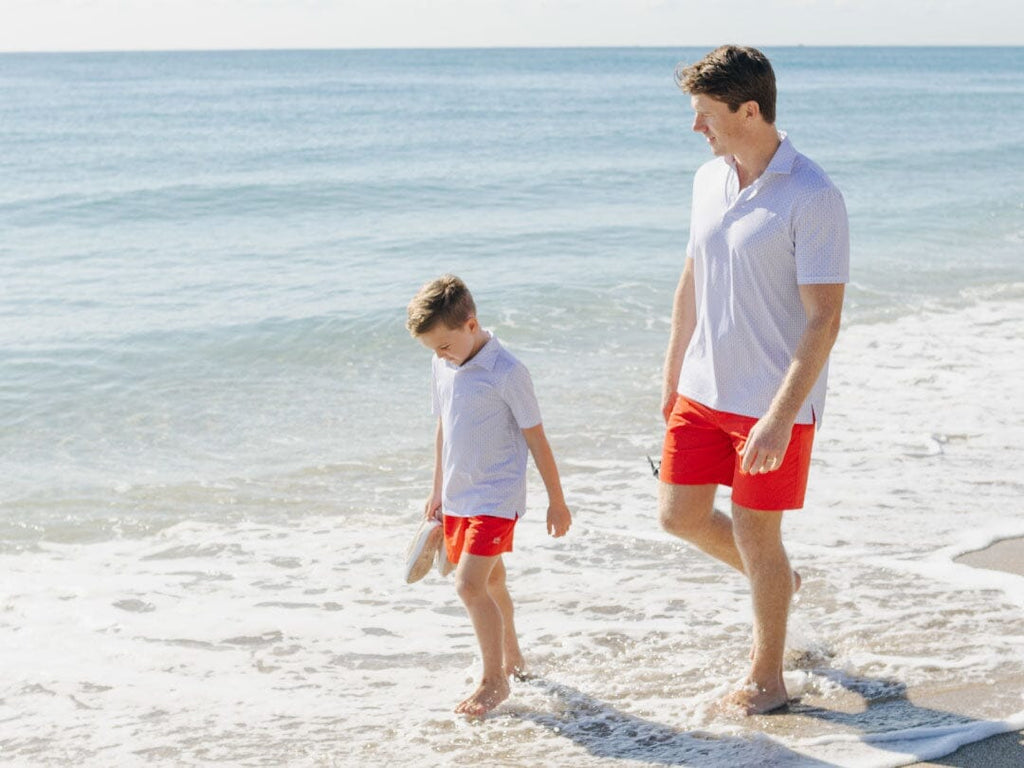 Father and son sitting on the beach wearing matching shirts.