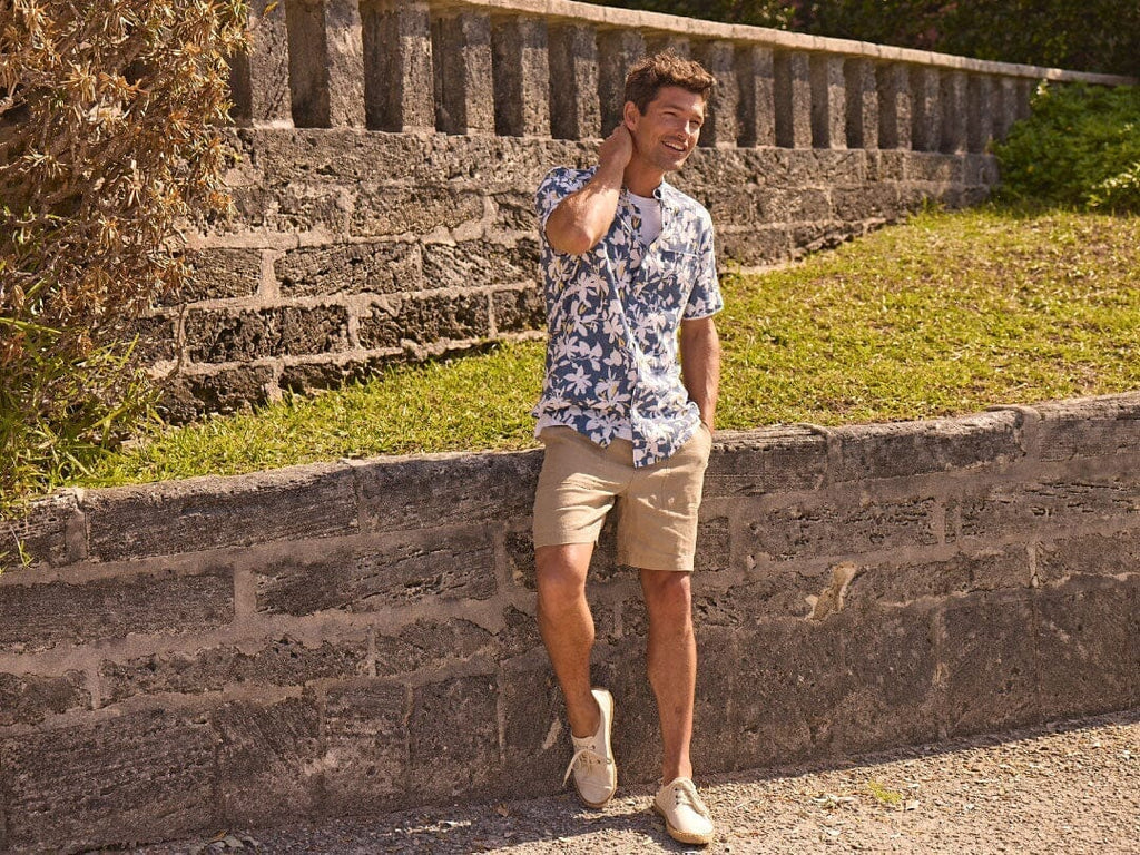 Man wearing printed short sleeve button down sitting in a chair outside.