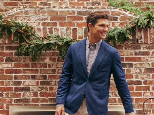 Man wearing a blazer and sport shirt outside holding a drink.