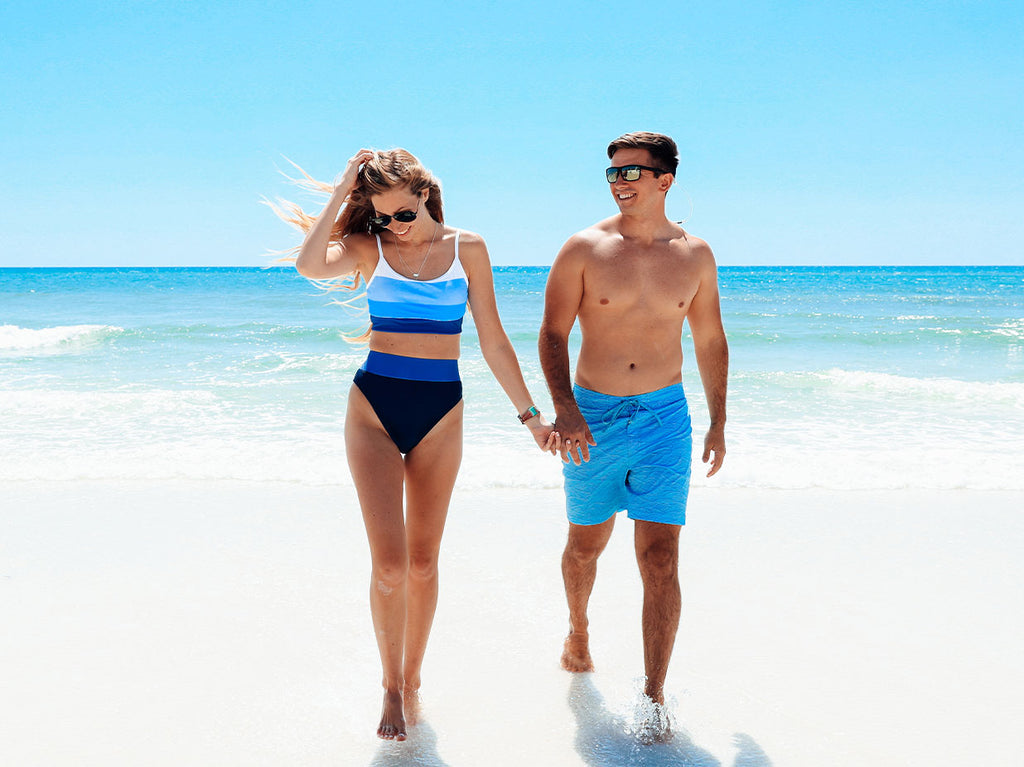 Man and woman walking on beach in swimwear.