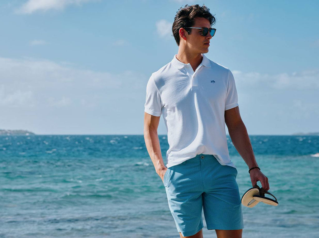 Man wearing white Skipjack polo and T3 gulf shorts on the beach.