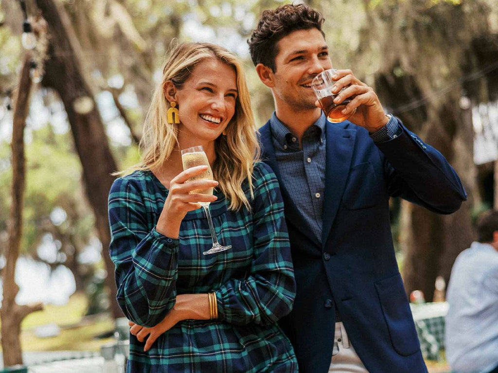 Woman and man holding champagne in holiday outfits outside.