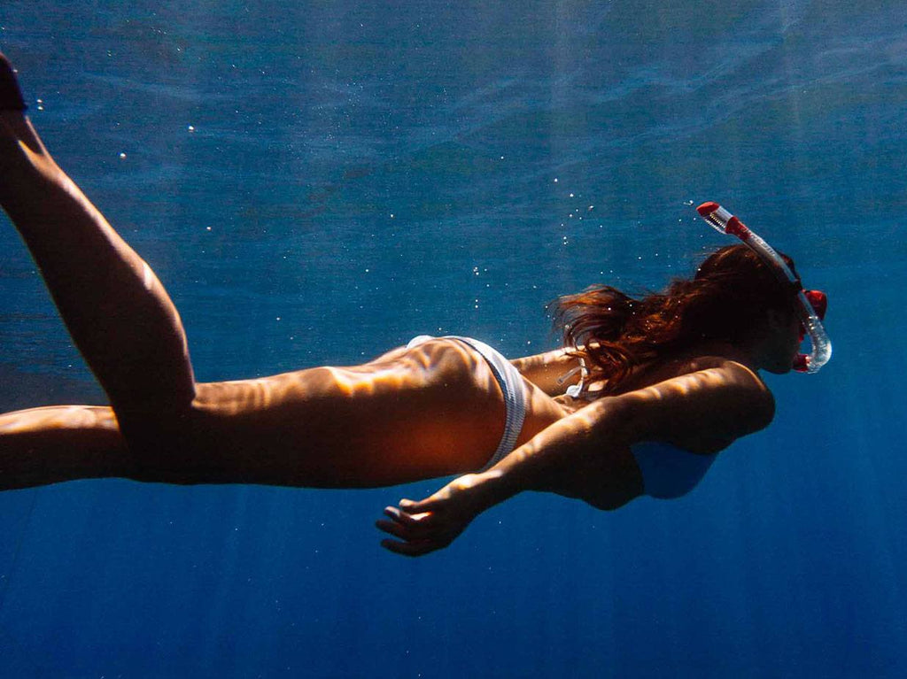 Woman swimming in ocean away from camera.