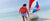 Man in red hoodie and swim trunks on the beach.