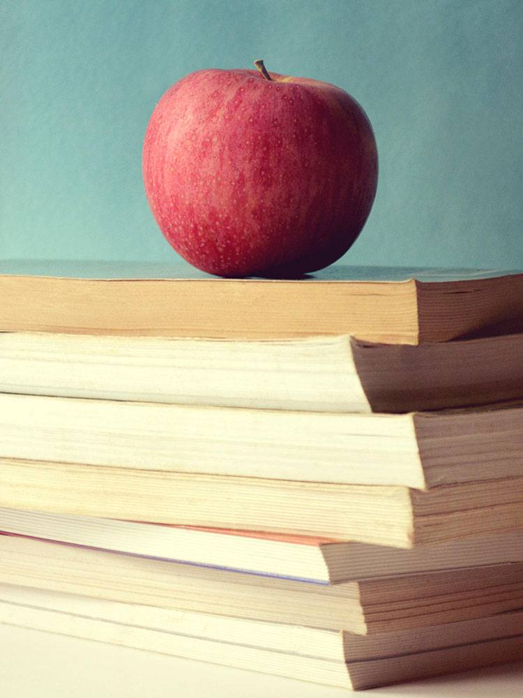stack of books on teacher's desk with apple on top